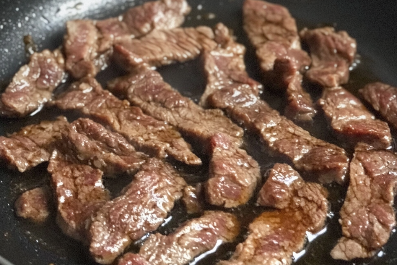 Tender beef slices and onions cooking in a skillet